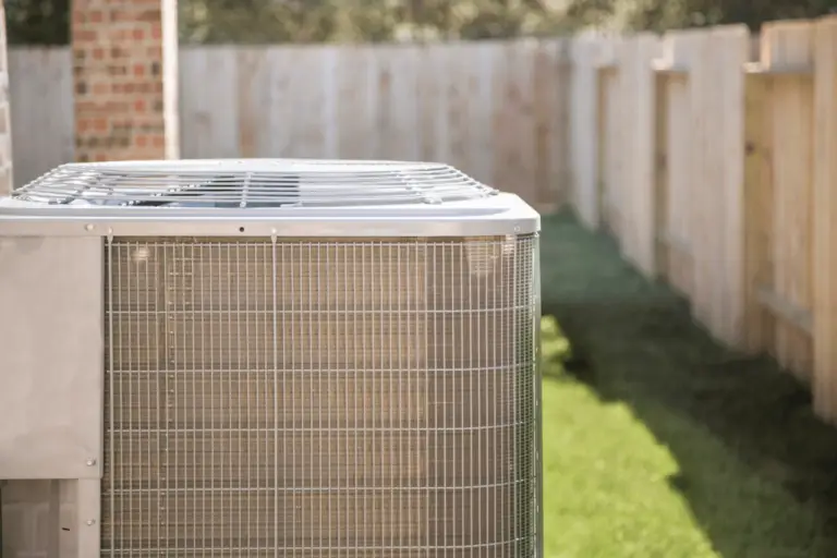 Central air conditioning unit in a nice-looking side yard. Brick column and wooden fence seen in the background. ATTYX HVAC