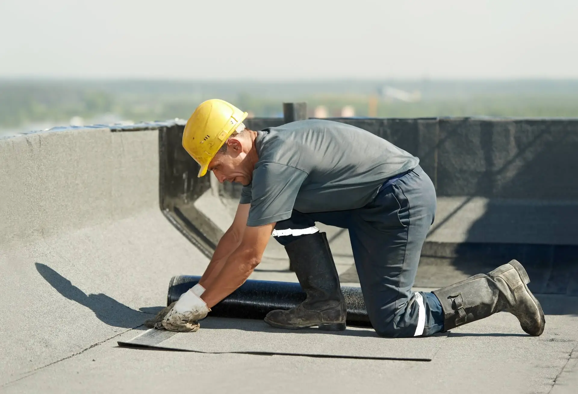 Roofer with safety hat installing new roofing material on flat roof. ATTYX Roofing