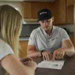 Salesman explaining the benefits of ATTYX with a potential customer in her home. ATTYX Roofing and Solar